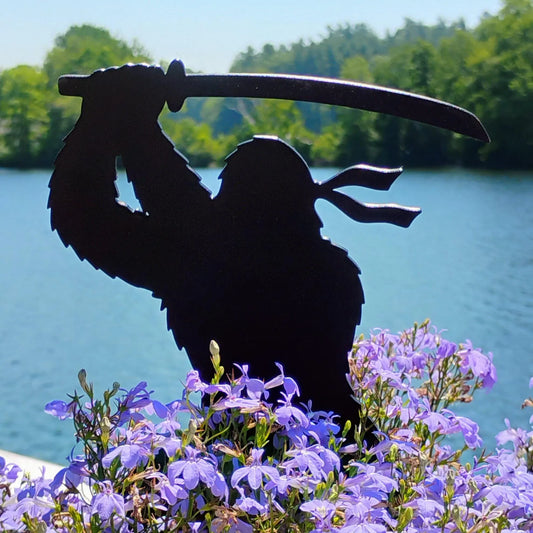 Bladefoot Ninja Bigfoot garden decoration holding a large sword above purple flowers beside a lake.