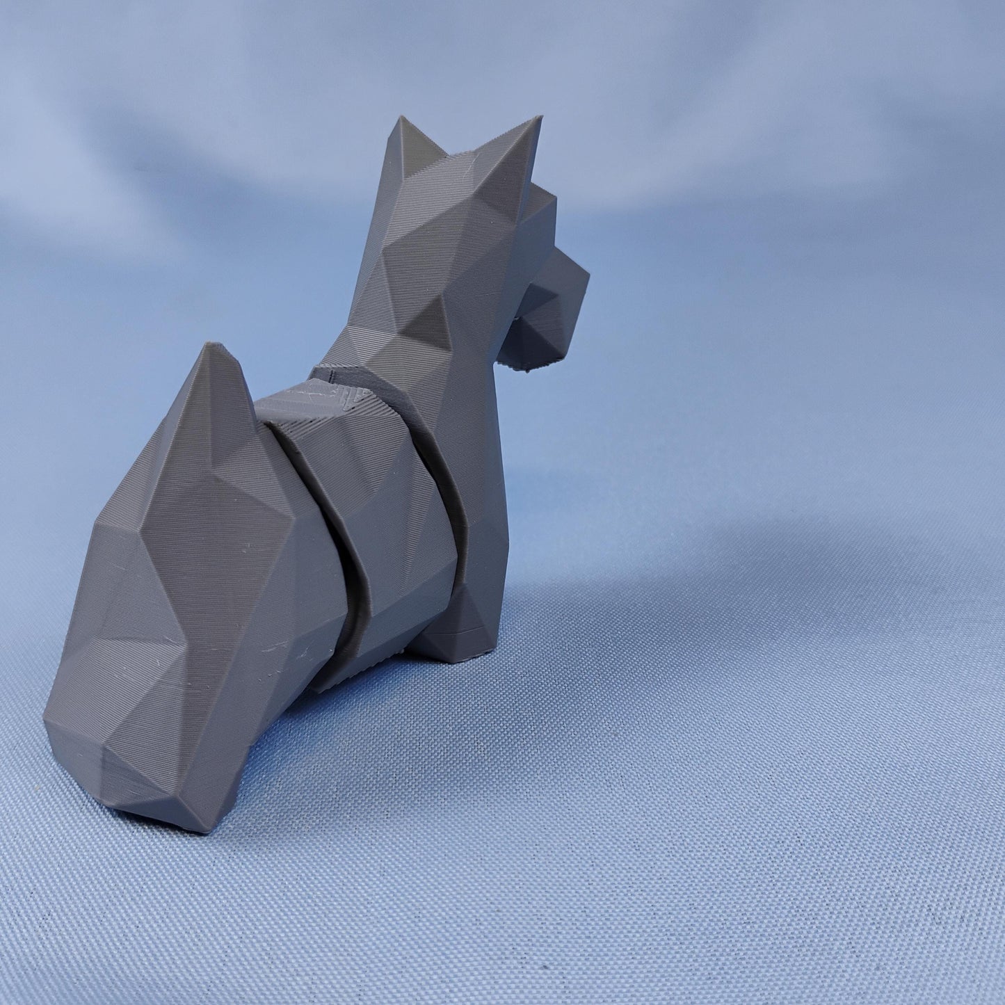 Back view of a gray flexi Scottie dog figurine showing articulated body sections, pointed ears, and faceted low-poly design.