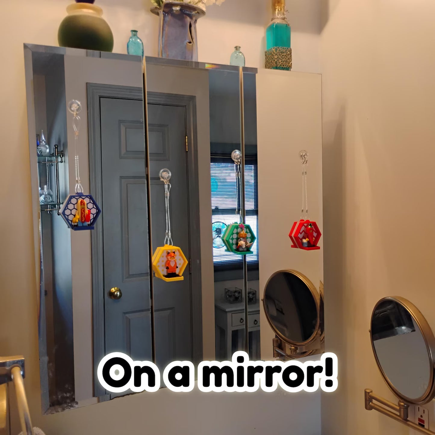 Colorful hanging minifigure displays attached to a mirror with suction cups, showing a fun display option for LEGO® figures.
