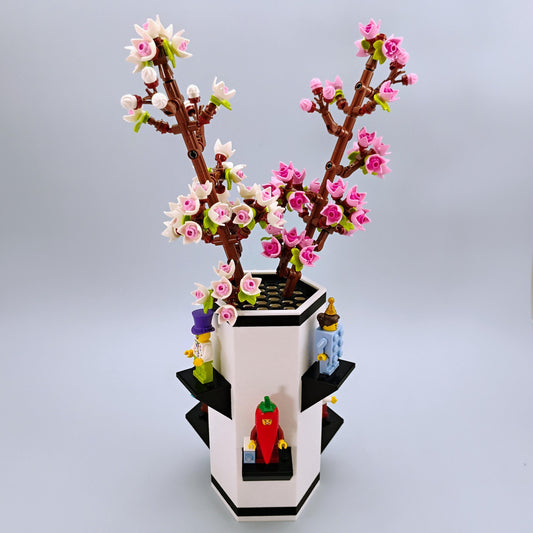 LEGO model of a cherry blossom in a Max Gallows Botanical Vase with LEGO figures displaued around it on a light gray background