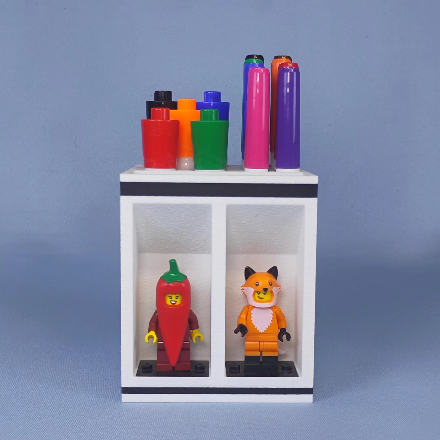 Front view of a white dry erase marker holder with large and fine-tip markers organized on top and two LEGO® minifigures displayed below.