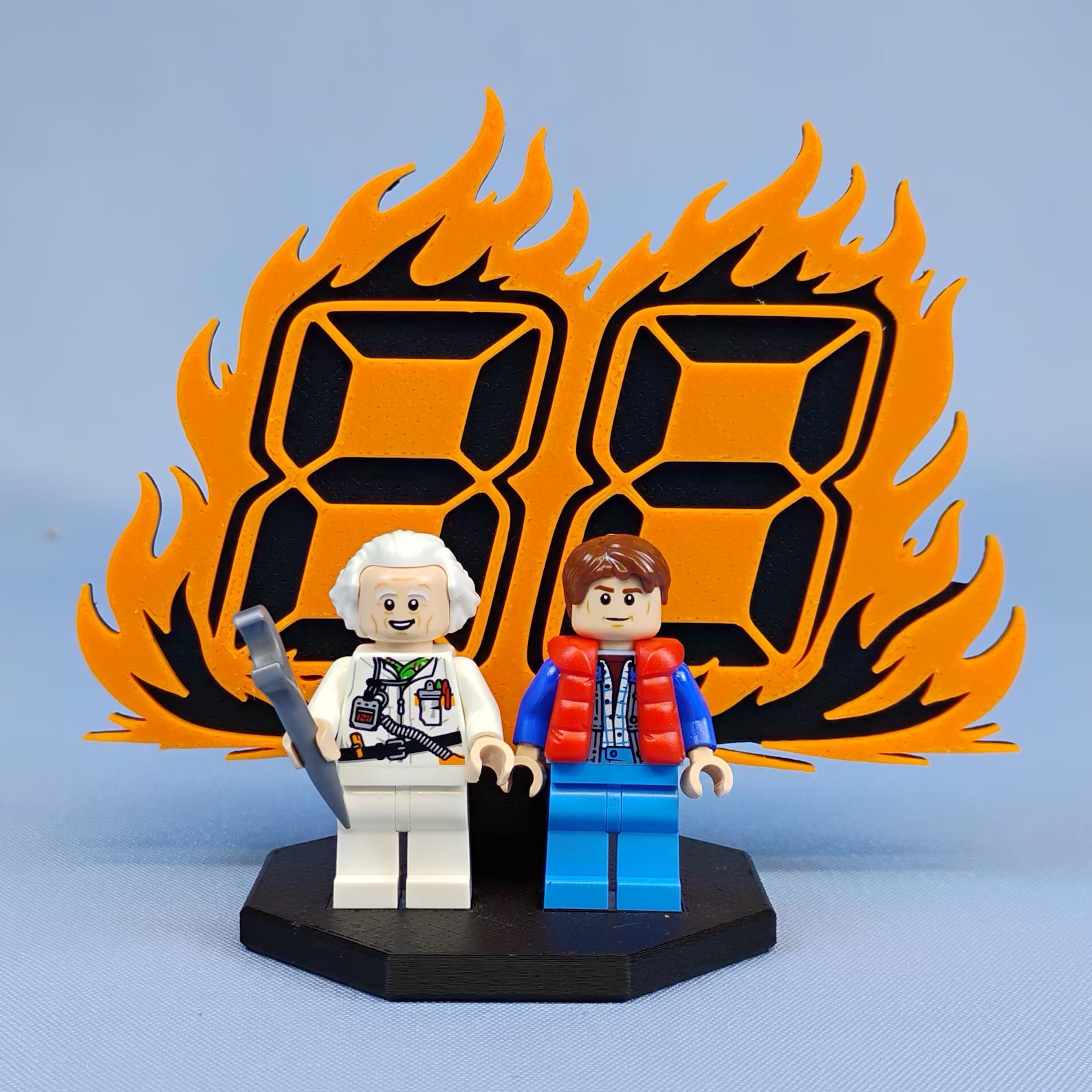 Front view of the Back to the Future 88 MPH flame display stand with two LEGO® minifigures on a black base.