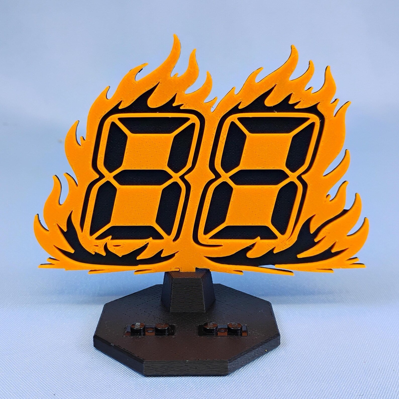 Back to the Future 88 MPH flame backdrop shown with black minifigure display base and support piece against a blue background.