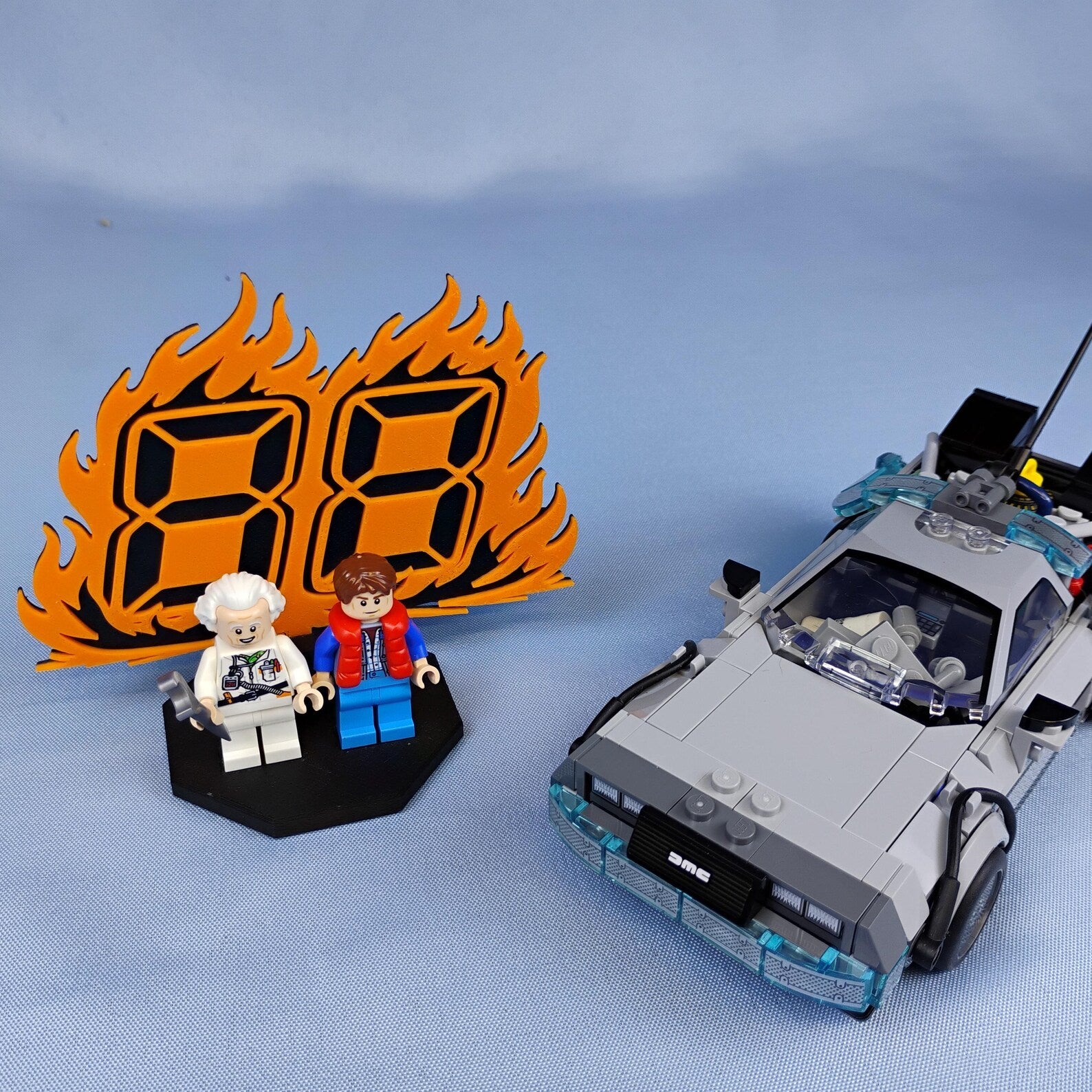 Back to the Future minifigure display with 88 MPH flame backdrop, two figures, and DeLorean time machine build on a blue background.