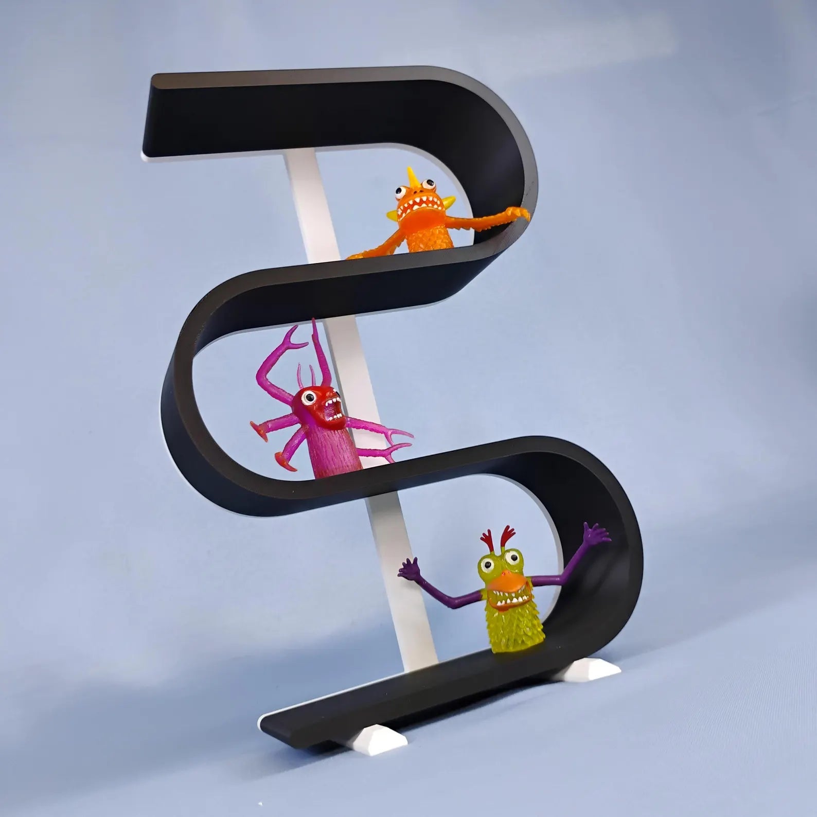 Angled view of a black squiggly display shelf with white supports and removable feet, styled with colorful miniature figures on its curved shelves.