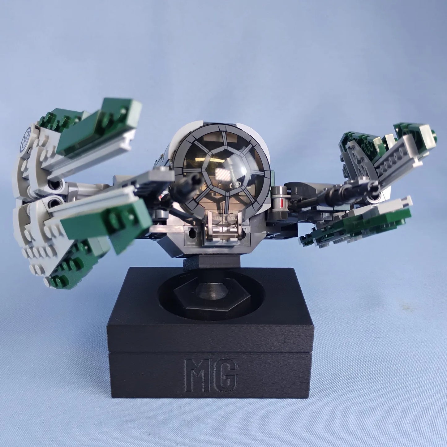 Black adjustable display stand for LEGO® ships with custom MG text printed on the front of the base.