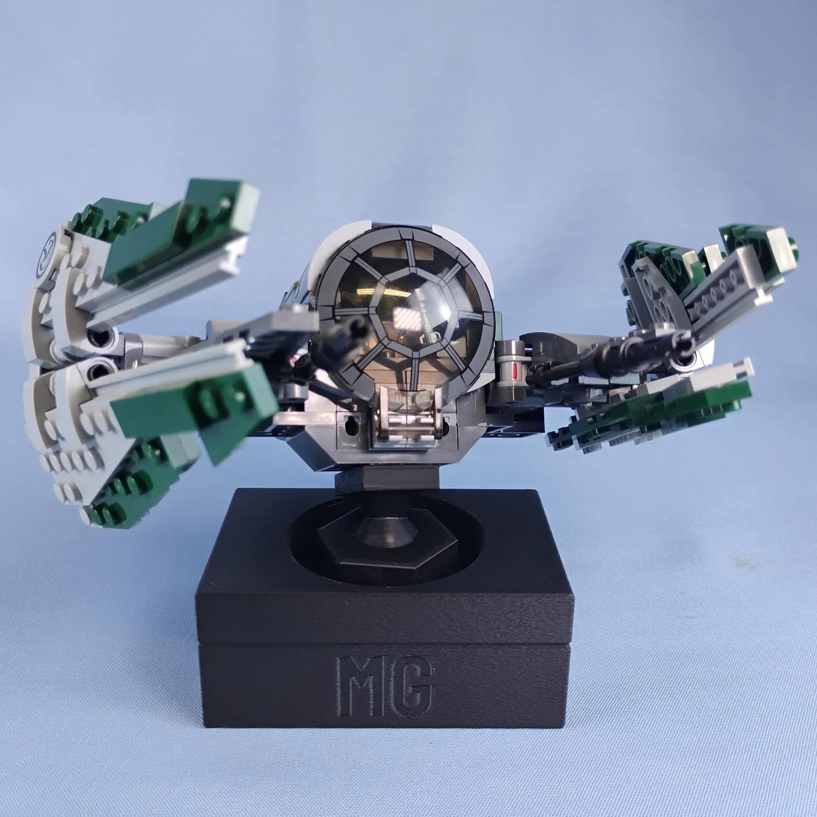 Black adjustable display stand for LEGO® ships with custom MG text printed on the front of the base.