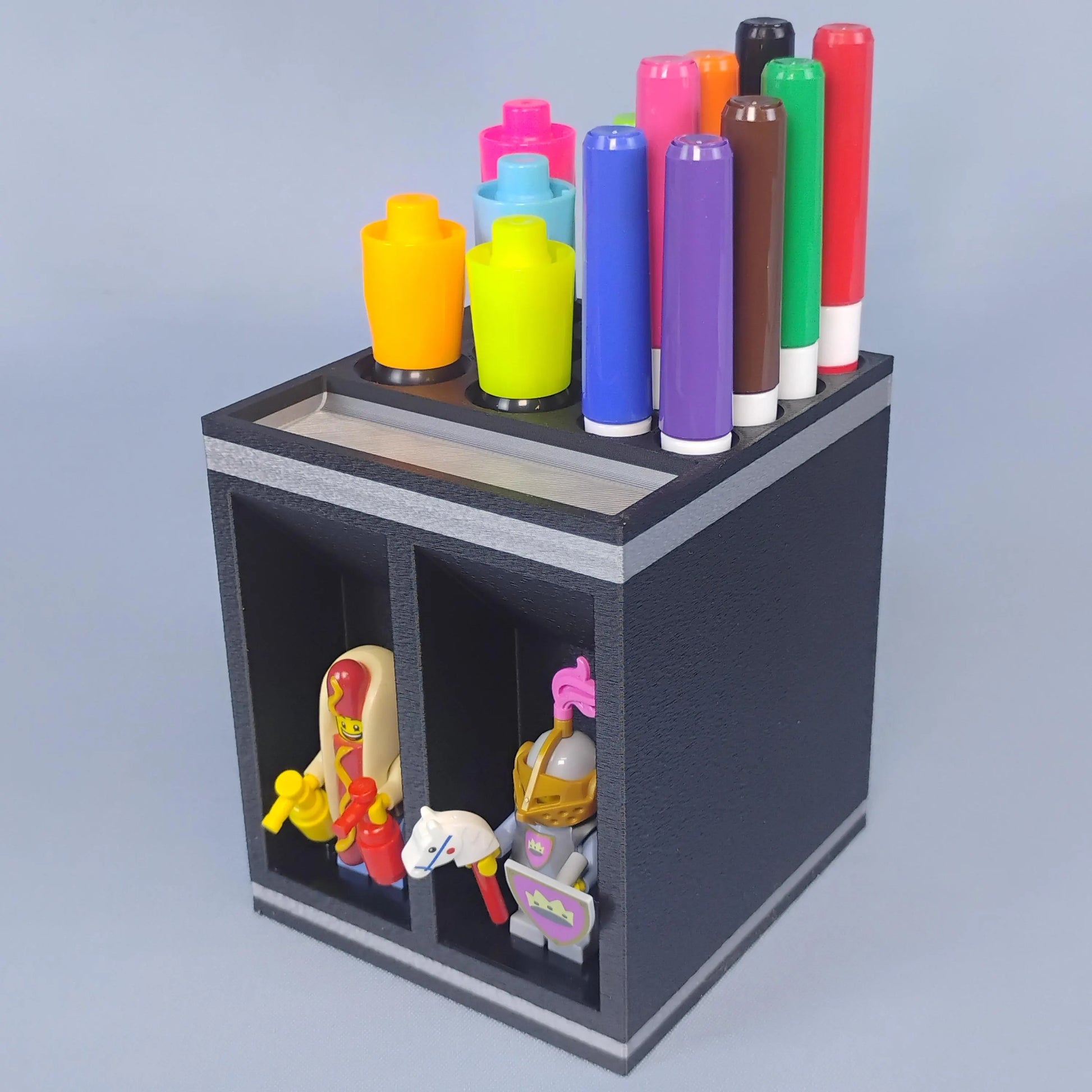 Angled view of a black dry erase marker holder with colorful markers arranged on top and two LEGO® minifigures displayed in the front compartments.