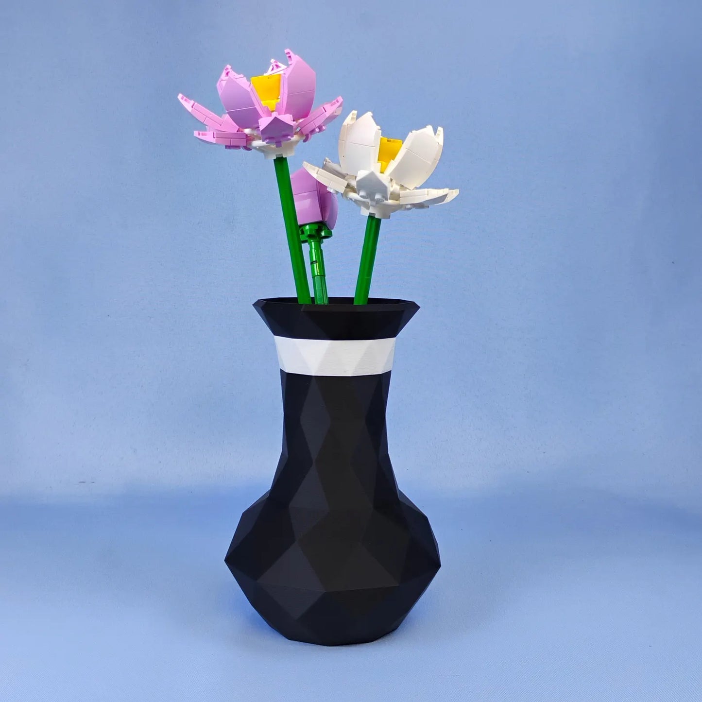 Black geometric vase holding LEGO® lotus flowers on a blue background