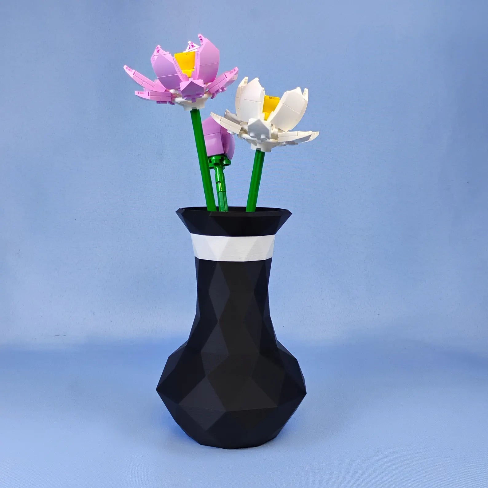 Black geometric vase holding LEGO® lotus flowers on a blue background