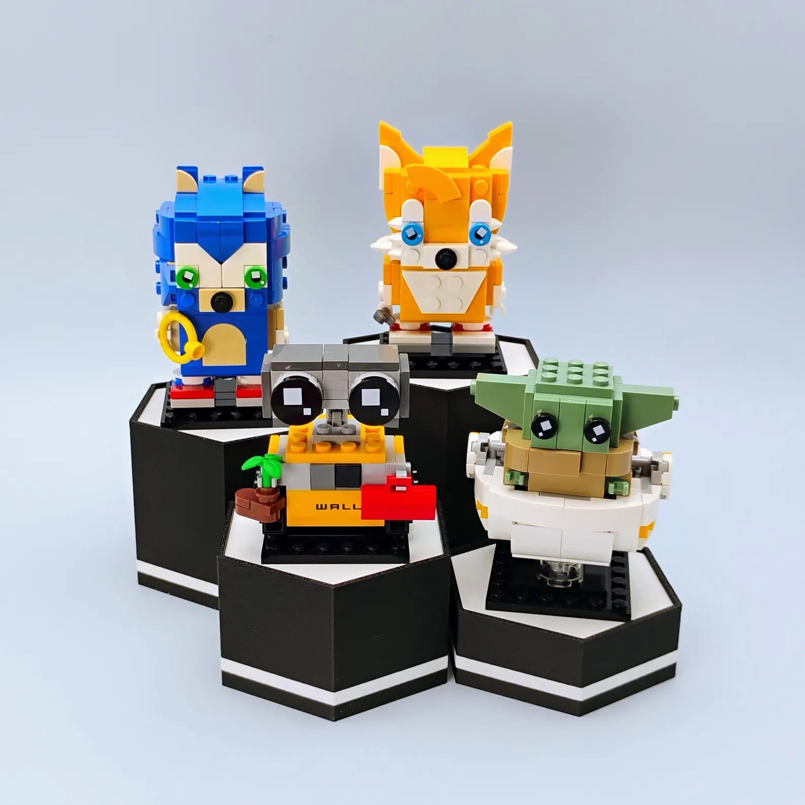 Black hex display stands with white accents shown holding LEGO® BrickHeadz-style figures in a layered shelf display.