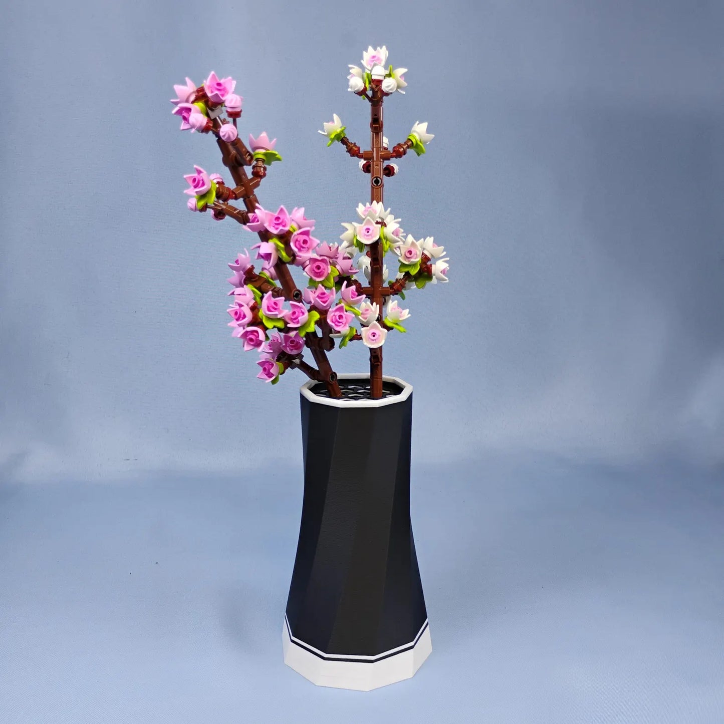 Black faceted vase displaying LEGO® Botanical cherry blossom branches with white accent base, shown as simple modern flower decor.