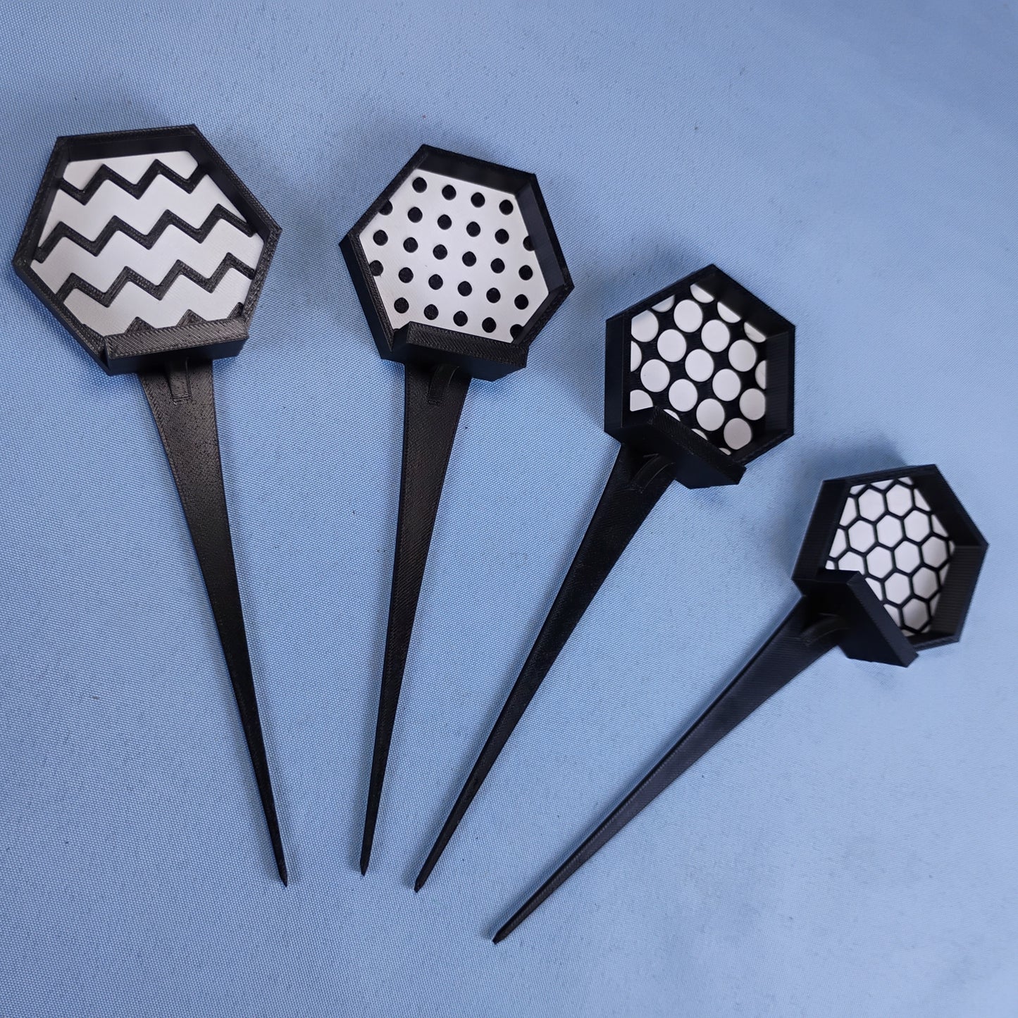 Four black LEGO® minifigure garden stakes showing the available zigzag, circle, studs and hexagon background patterns.