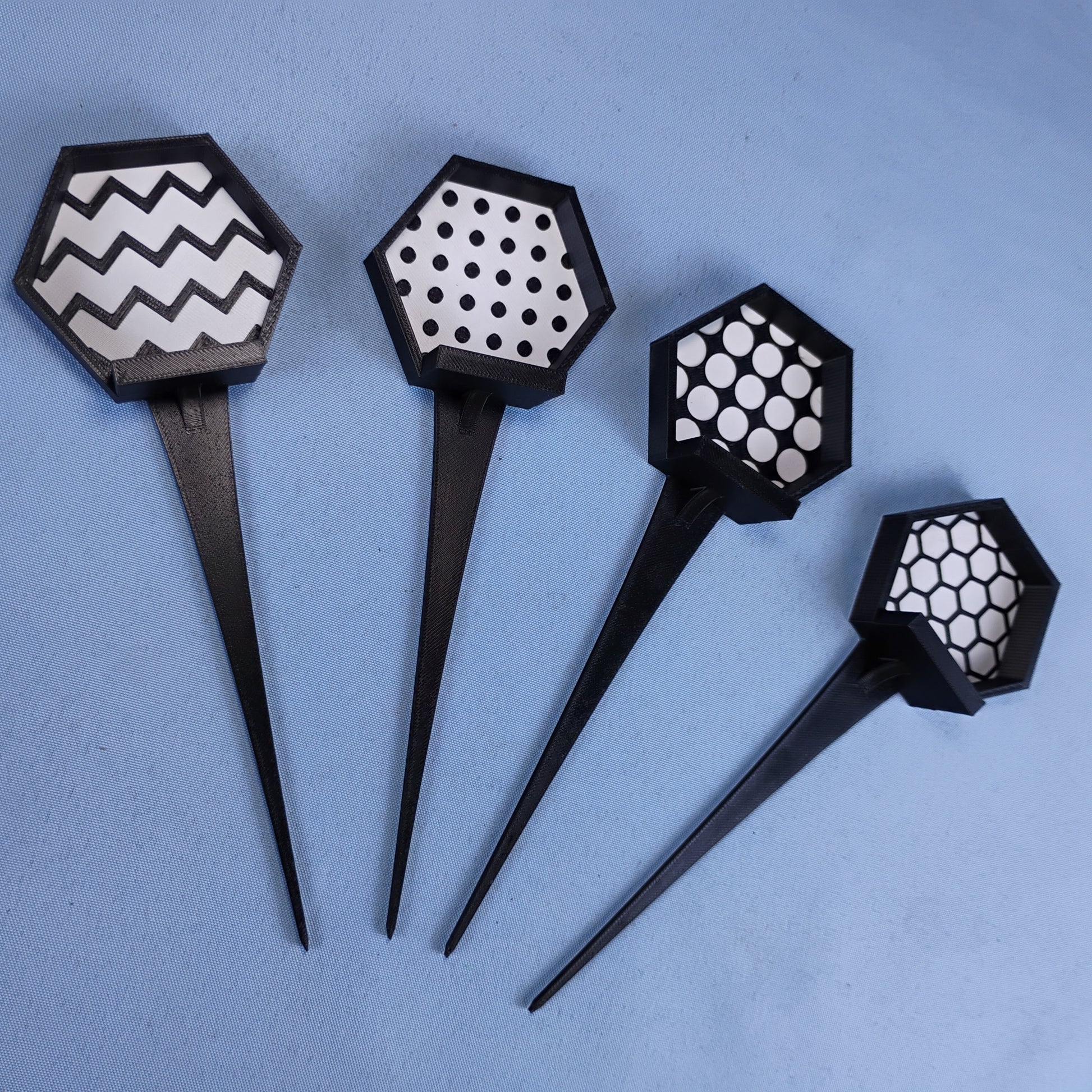 Four black LEGO® minifigure garden stakes showing the available zigzag, circle, studs and hexagon background patterns.
