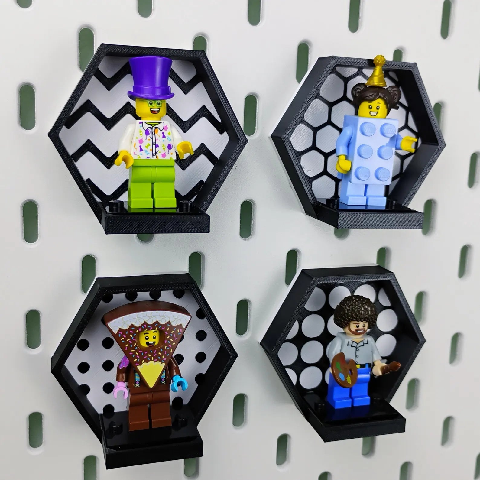 Four black SKÅDIS-compatible hexagon displays on a pegboard, each holding a LEGO® minifigure with a different patterned background.