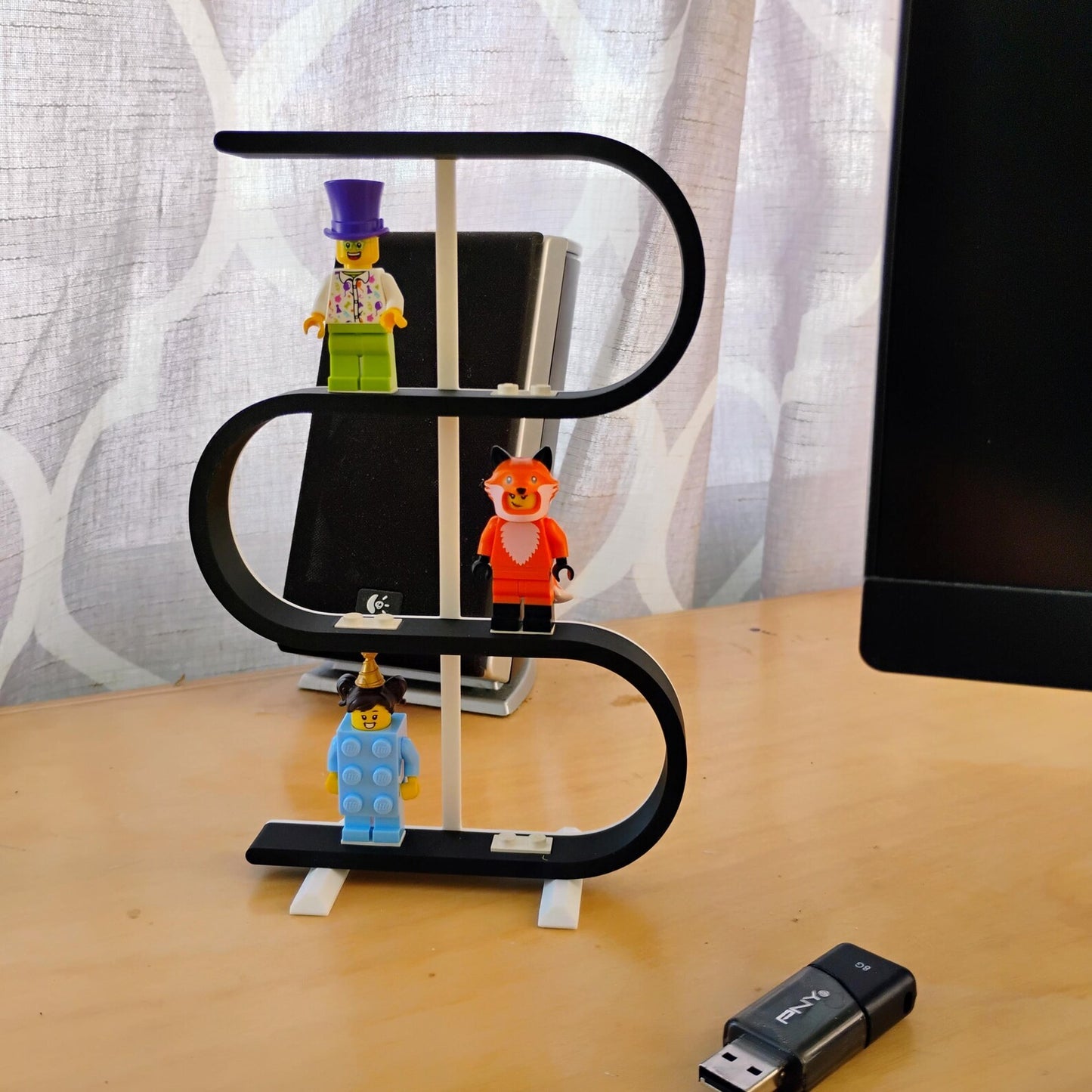 Black squiggle display stand holding LEGO® minifigures on a desk