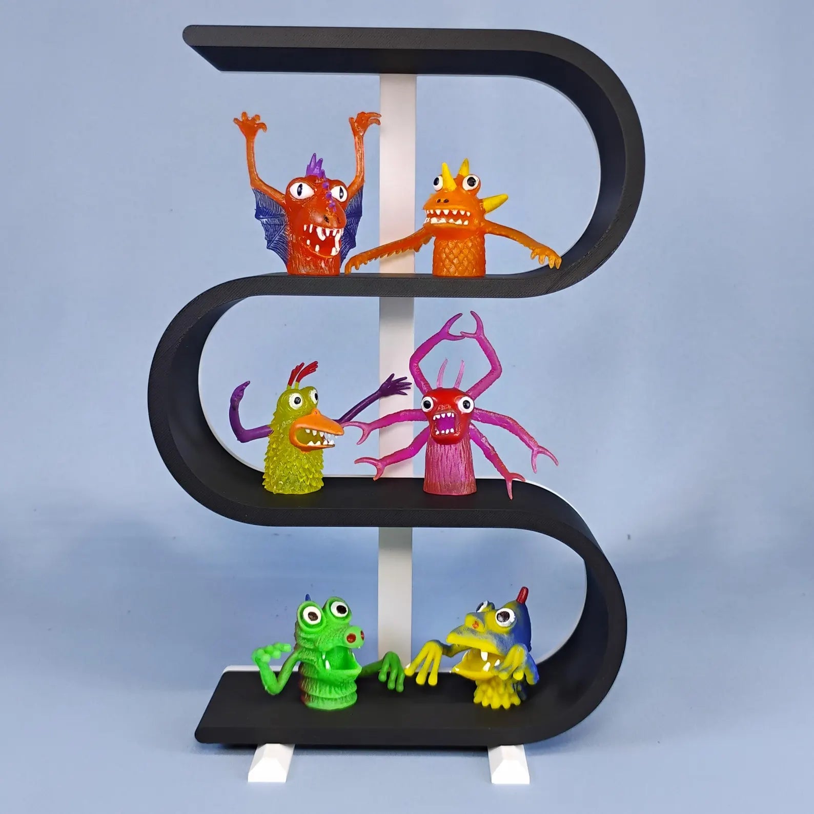 Black three-tier squiggly shelf with a white center support, removable feet, and colorful mini monster figures displayed on each curved level.