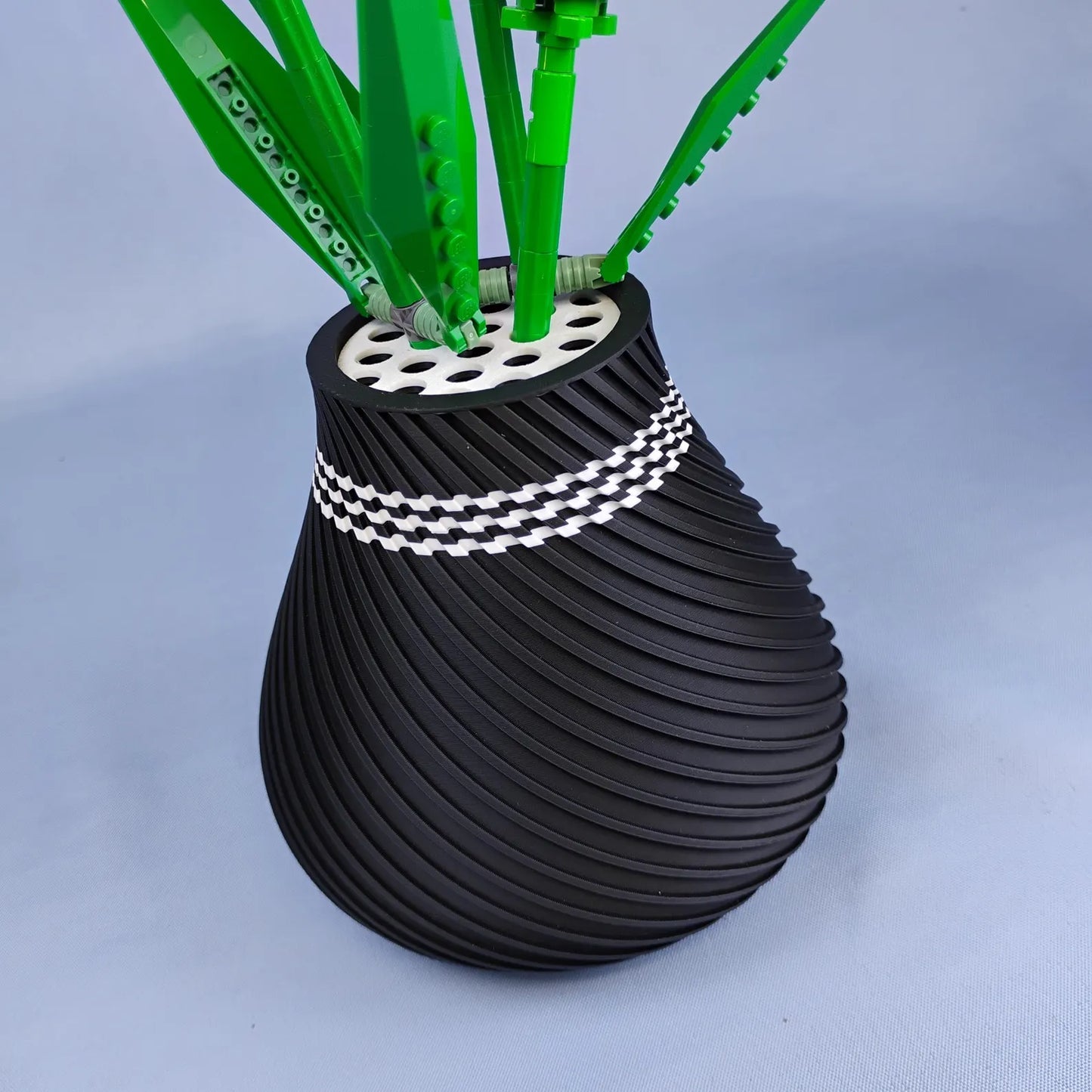Black swirly vase holding LEGO® botanical stems in the removable grid insert