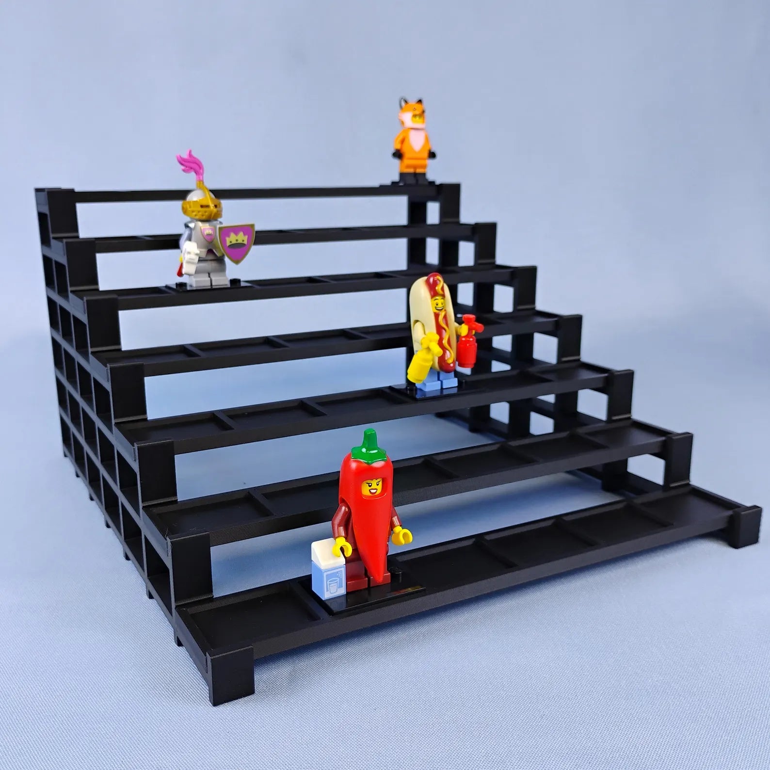 Black tiered display stand for LEGO® minifigures with several figures arranged across the stepped rows.