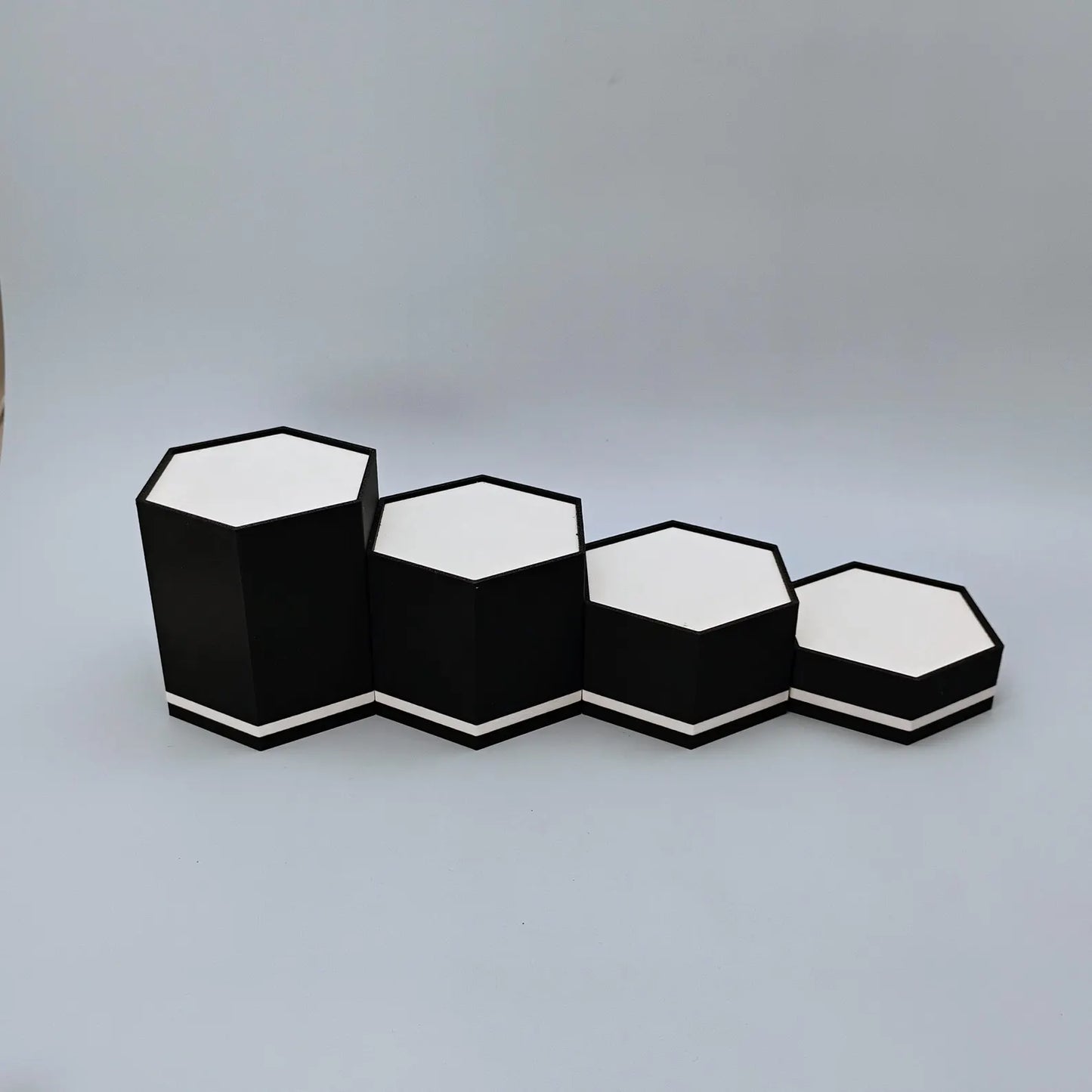 Empty black and white hex display stands lined up to show tiered height options for collectibles and figure displays.