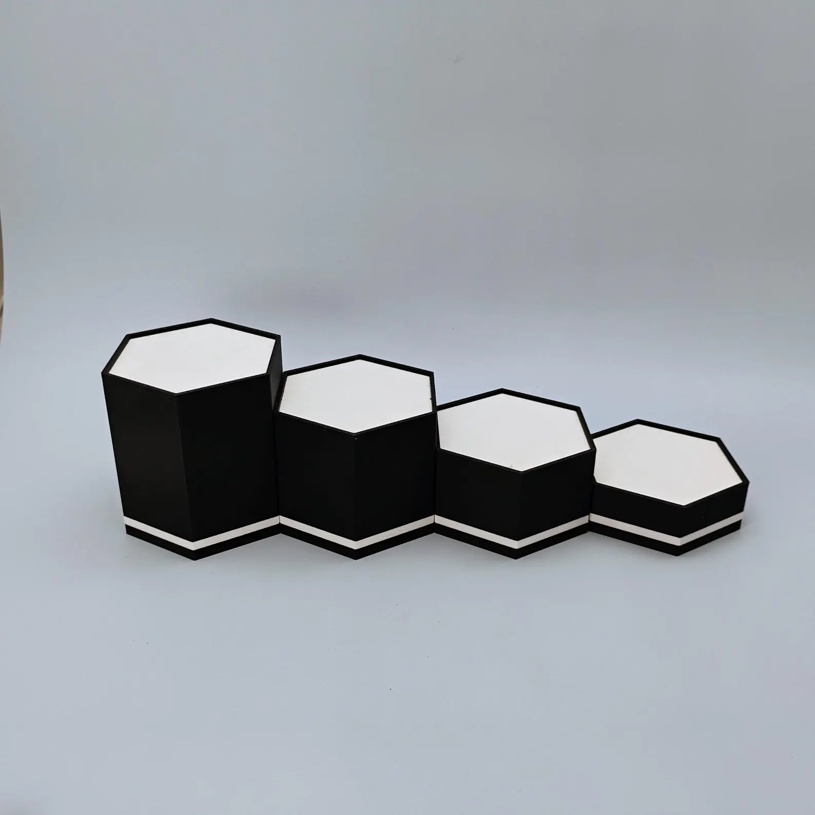 Empty black and white hex display stands lined up to show tiered height options for collectibles and figure displays.