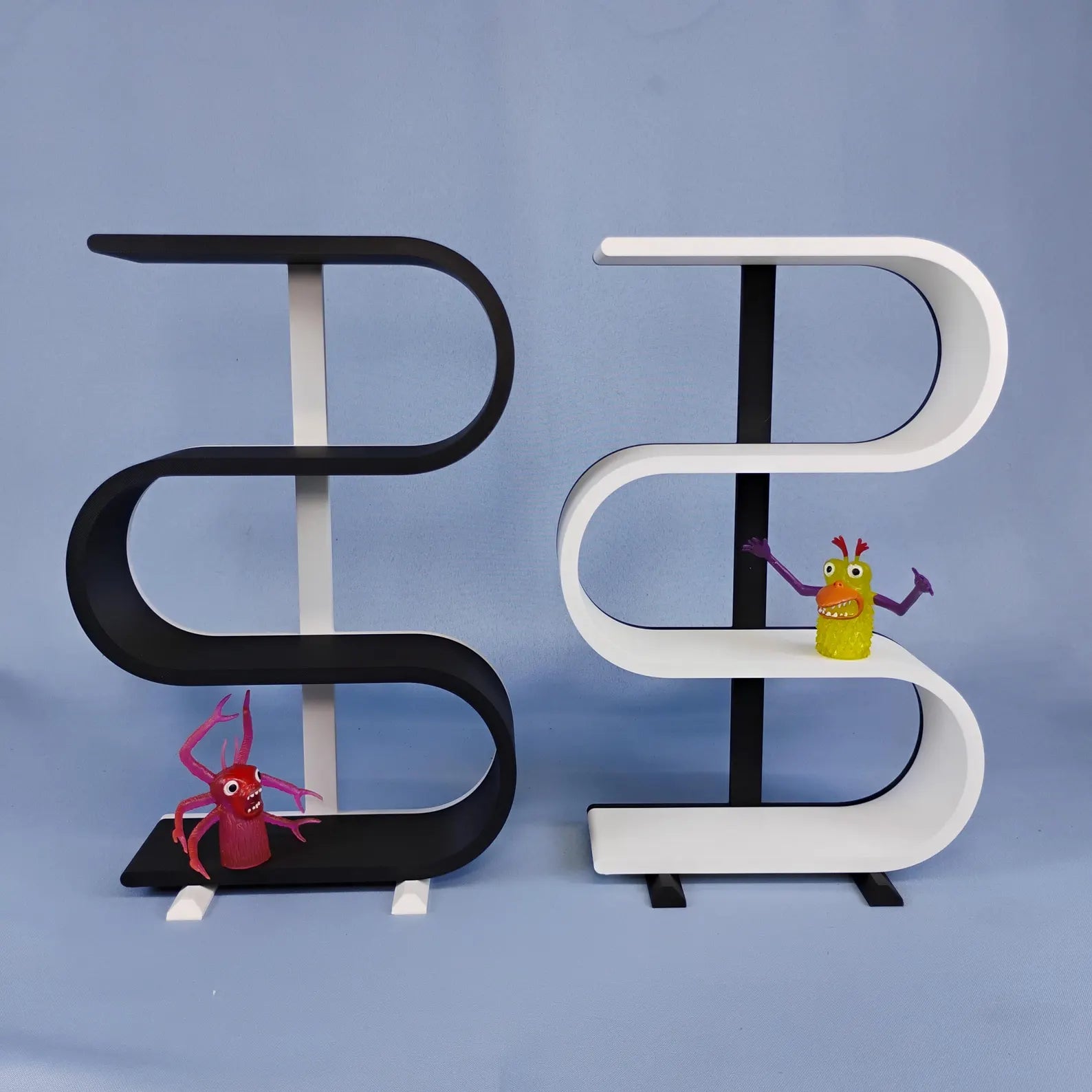 Black and white squiggly display shelves shown side by side for a color and size comparison, with removable feet and a few colorful miniature figures for scale.