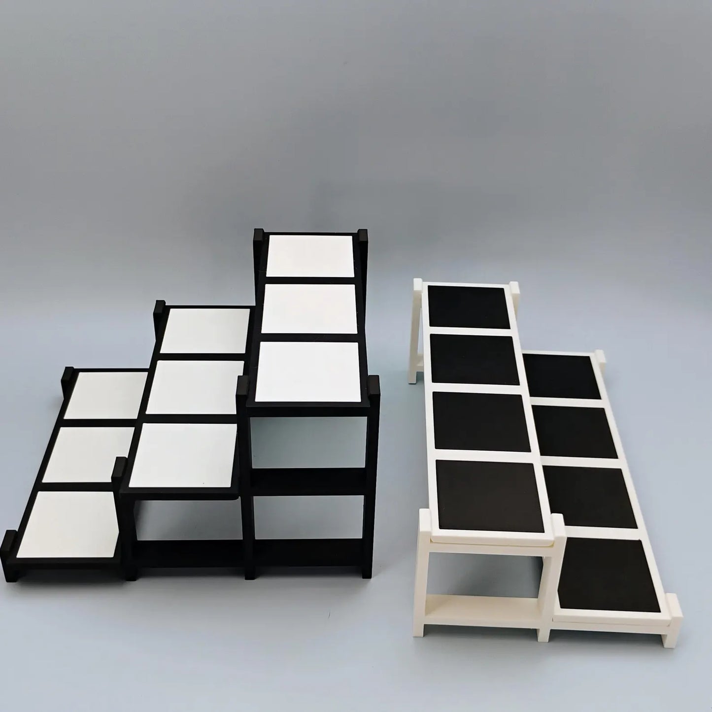 Black and white tiered display stands shown in different sizes with removable tiles for Funko Pops, trinkets, and collectibles.