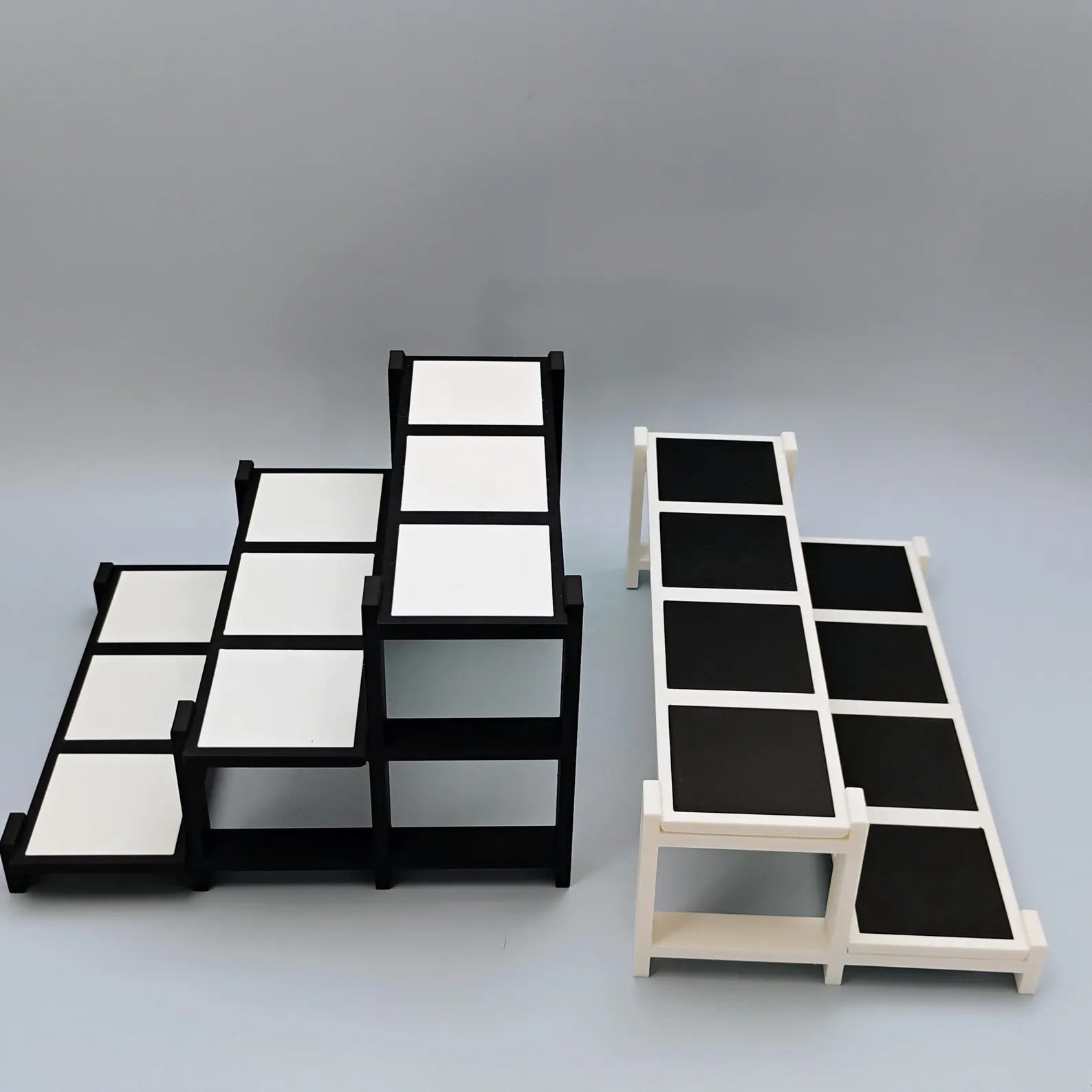 Black and white tiered display stands shown in different sizes with removable tiles for Funko Pops, trinkets, and collectibles.