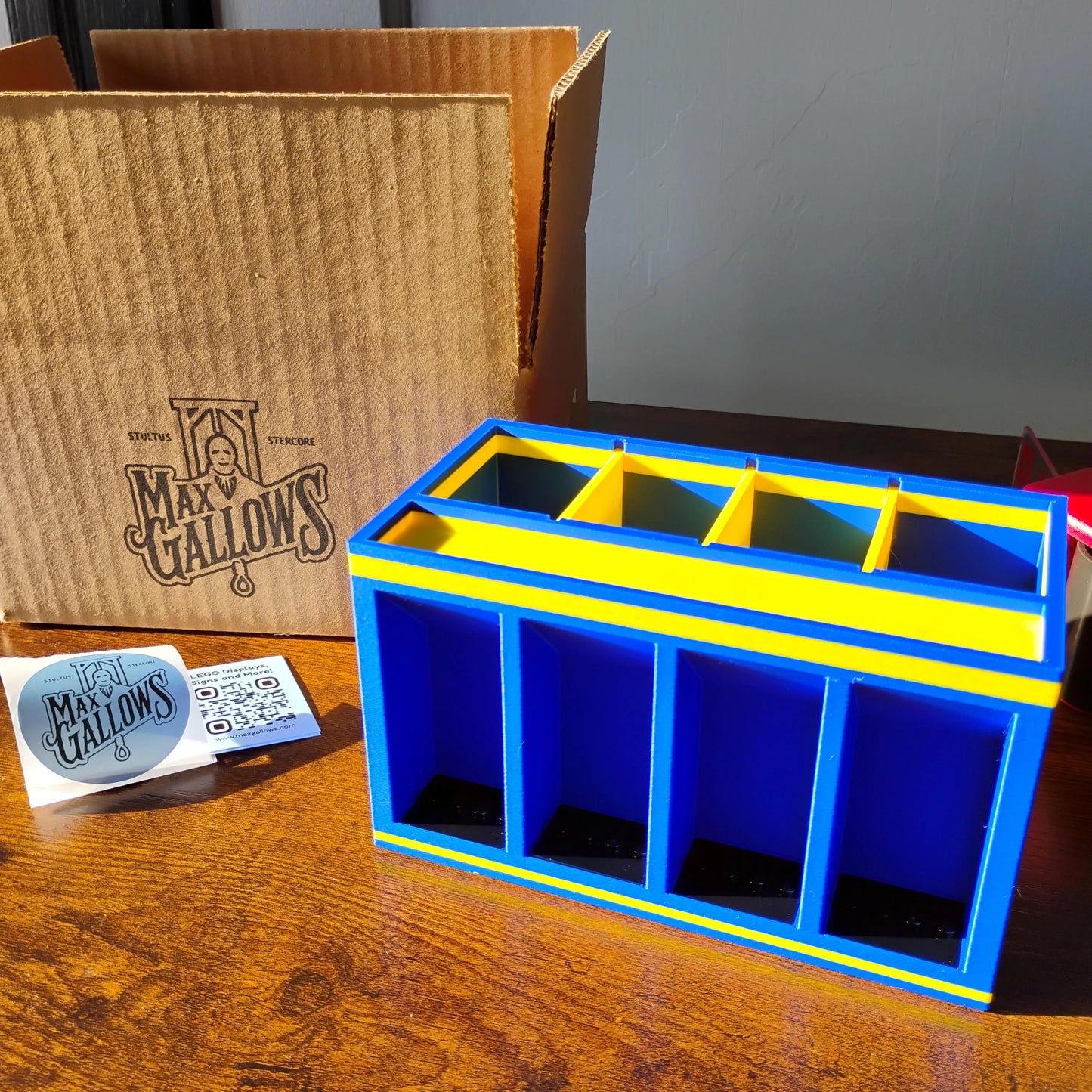 Blue and yellow Minifigure Desk Organizer Display with 'Max Gallows' branding on a shipping box surface