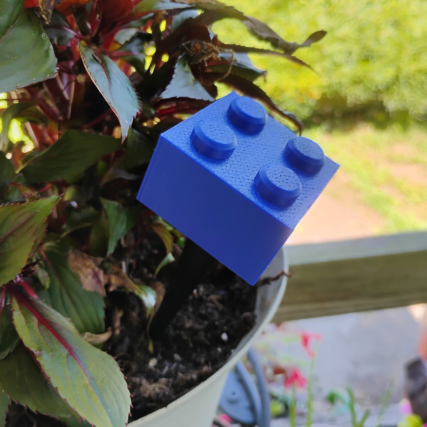 Blue building brick plant stake placed in a flowerpot to add playful building brick decor.