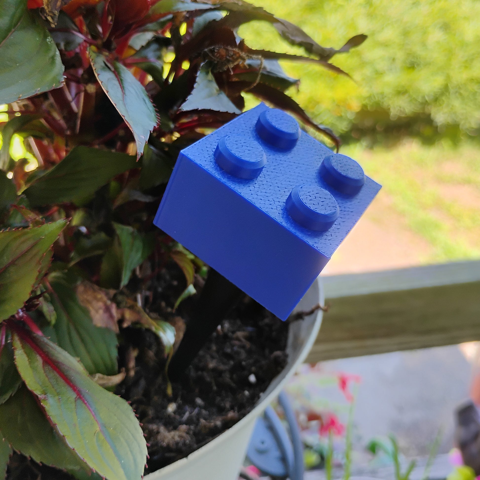 Blue building brick plant stake placed in a flowerpot to add playful building brick decor.