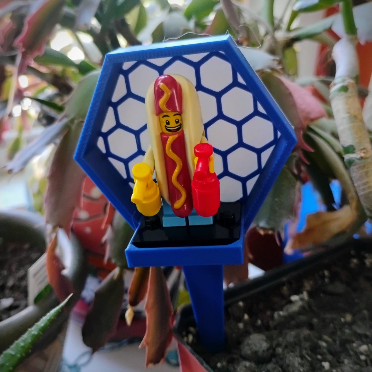 Blue hexagon LEGO® minifigure plant stake displayed in a houseplant with a hot dog minifigure.
