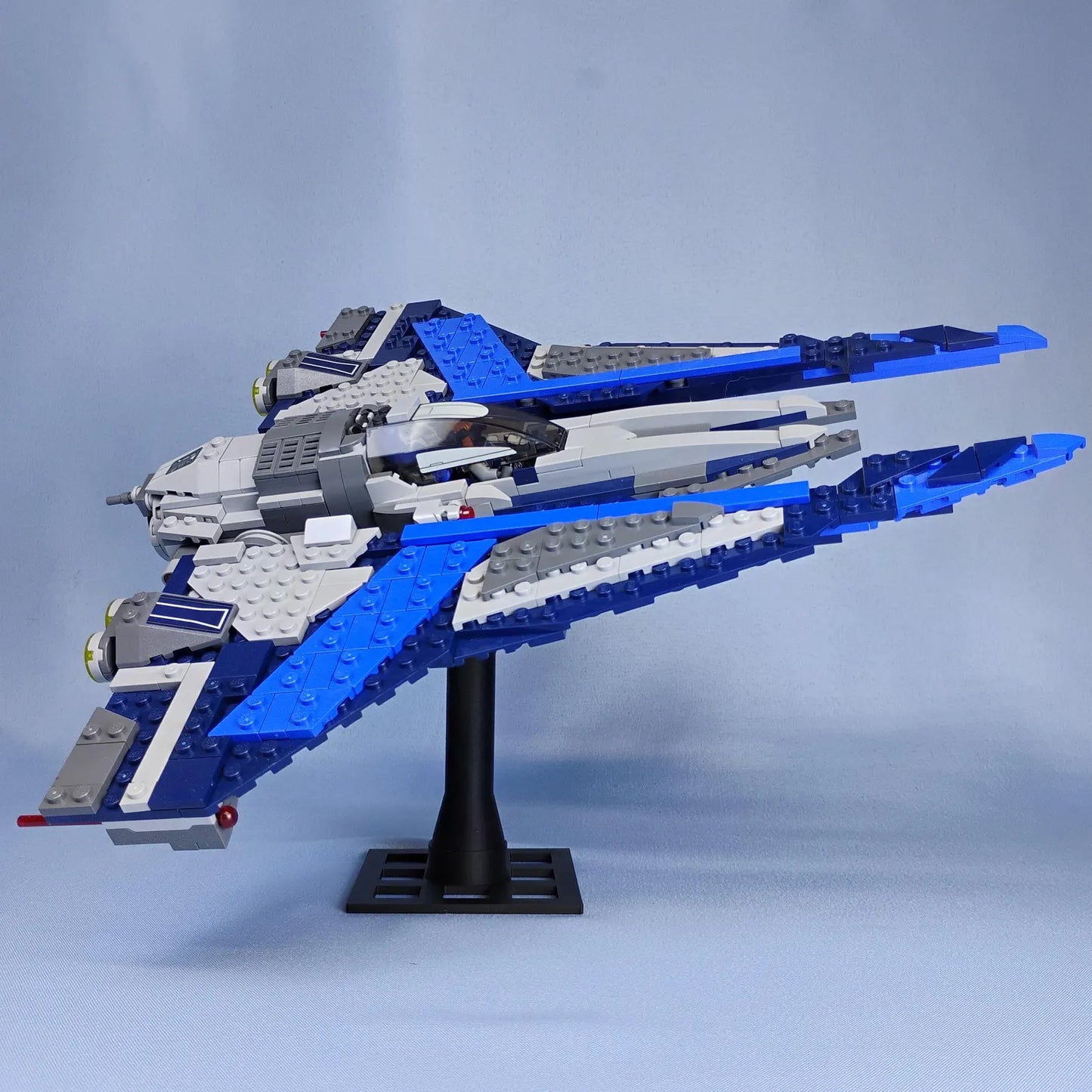 Blue LEGO® spaceship displayed on a black adjustable stand, posed at a clean side angle for desk or shelf display.