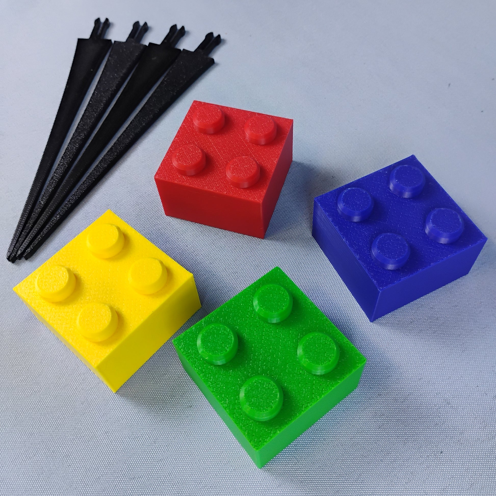 Red, blue, green and yellow removable building brick toppers shown beside four black plant stakes.