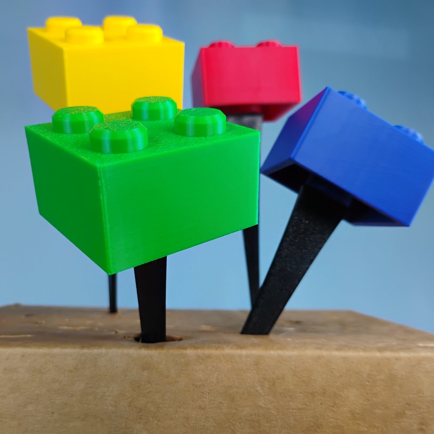 Colorful building brick plant stakes in red, green, blue and yellow with black 6-inch stakes.