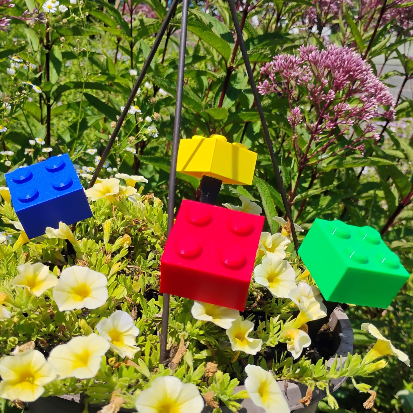 Red, blue, green and yellow building brick plant stakes adding colorful decor to an outdoor flower garden.
