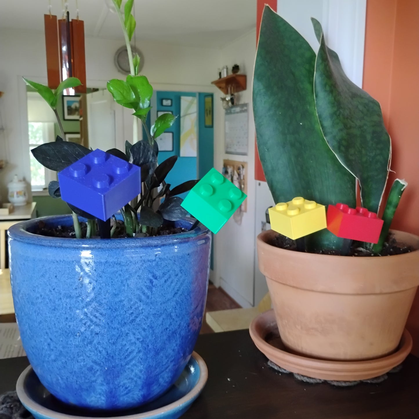 Blue, green, yellow and red building brick plant stakes displayed across two indoor houseplant pots.