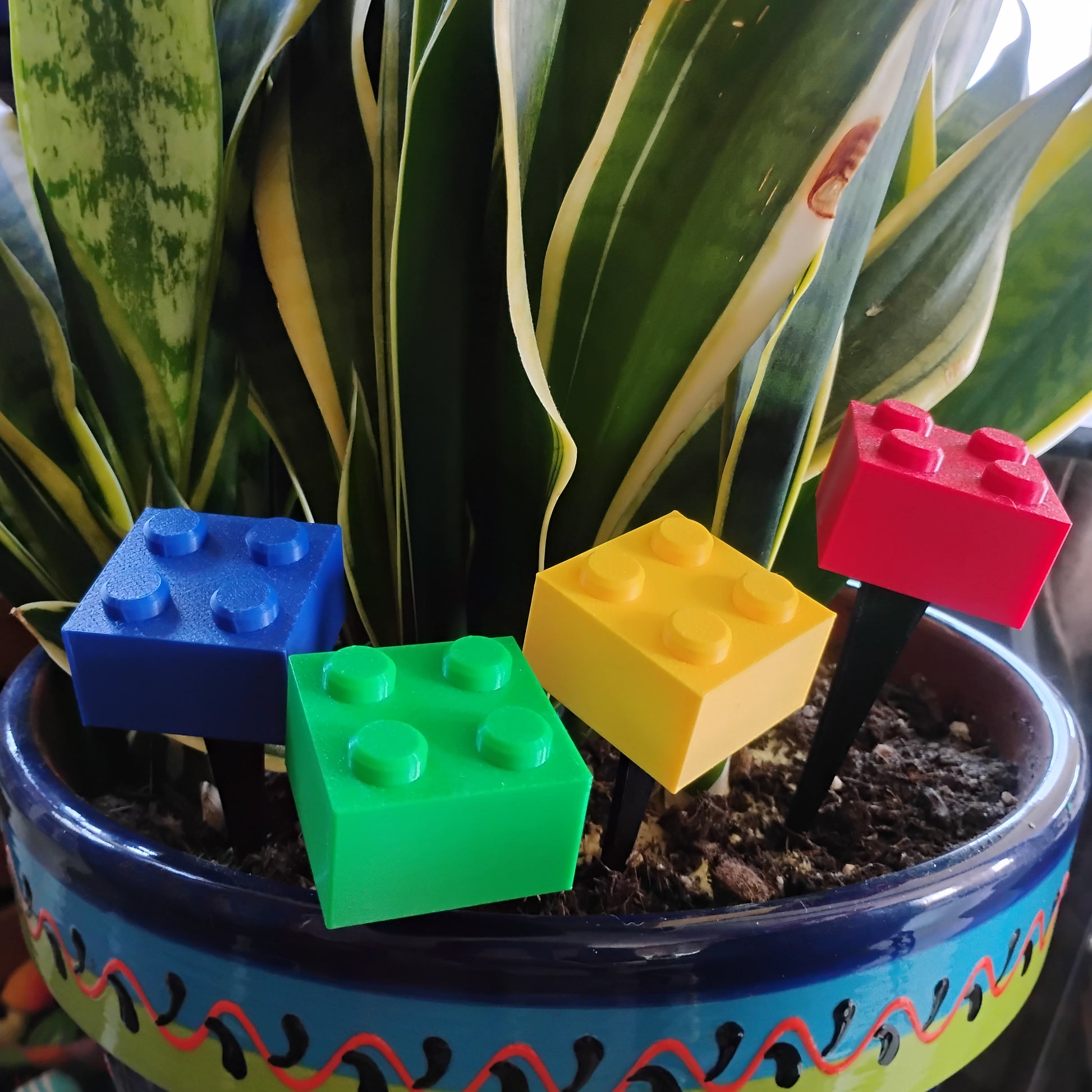 Colorful building brick plant stakes decorating a large indoor houseplant in a patterned ceramic pot.