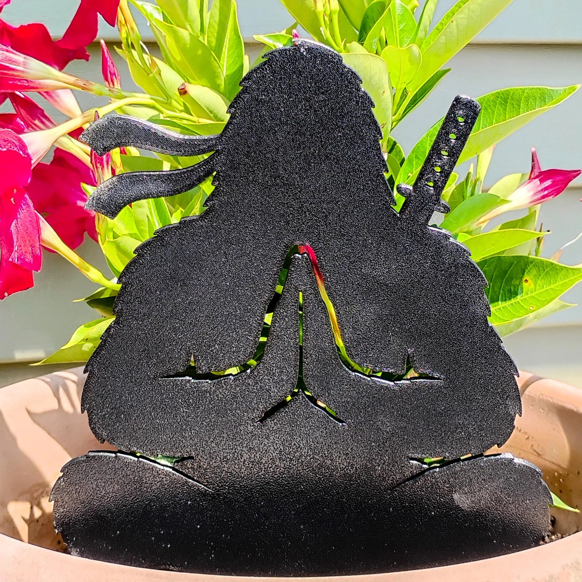 Calm Cryptid Ninja Bigfoot decoration sitting in meditation among bright pink flowers in an outdoor planter.