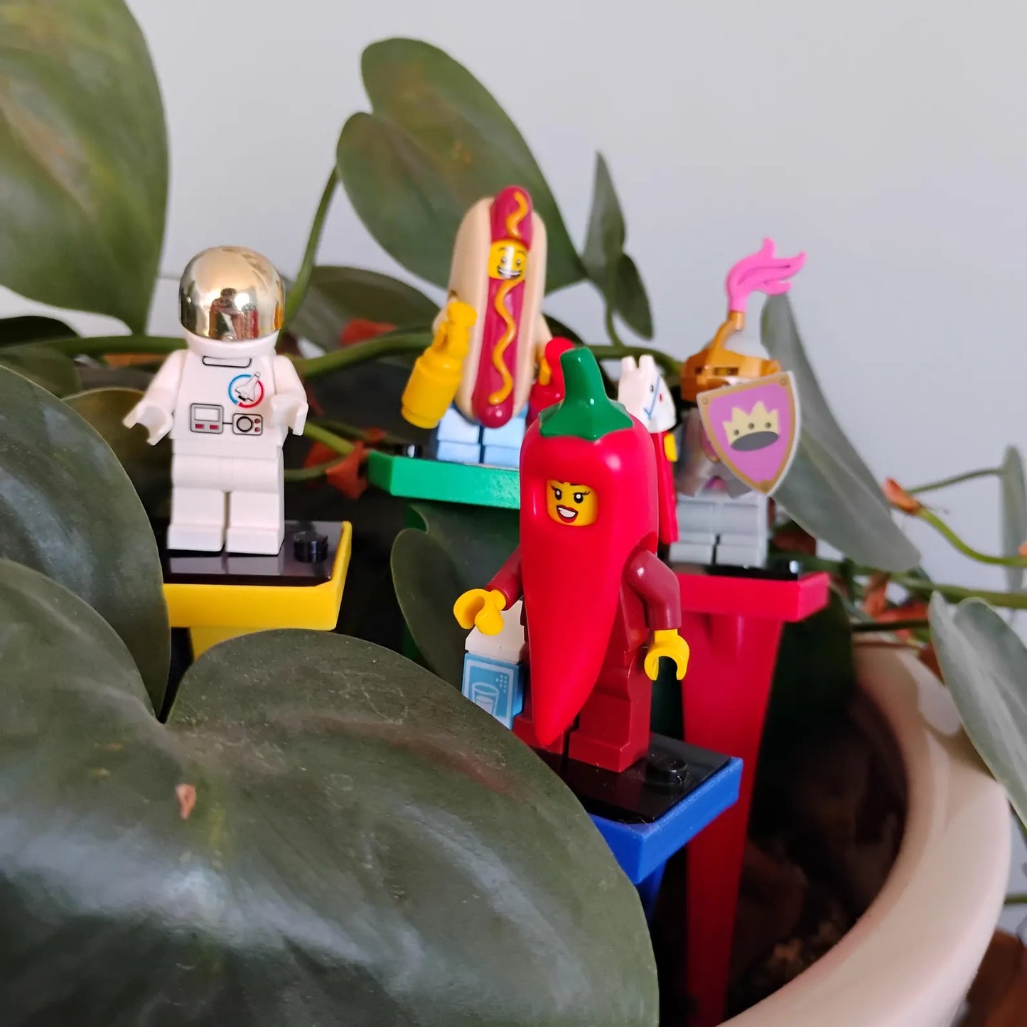 Colorful plant stakes holding LEGO® minifigures among indoor houseplant leaves