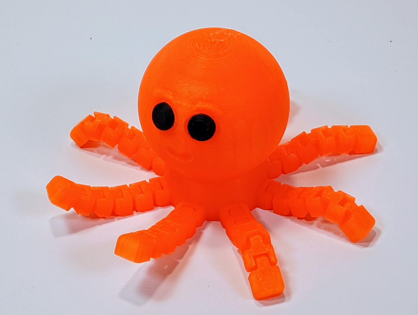 Cute orange flexi octopus figurine with eight bendy legs and black eyes, shown as a fun desk decor or fidget gift.