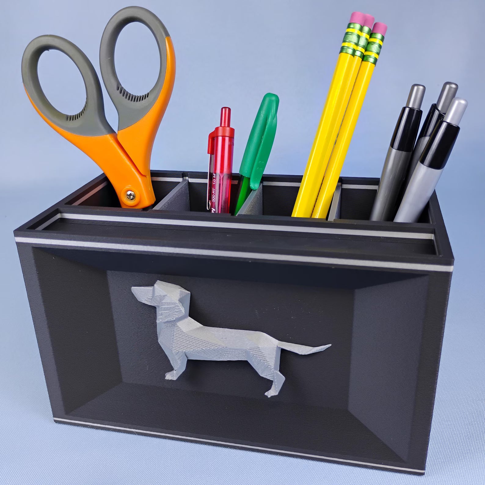 Gray Dachshund pencil holder with office supplies photographed on a blue background