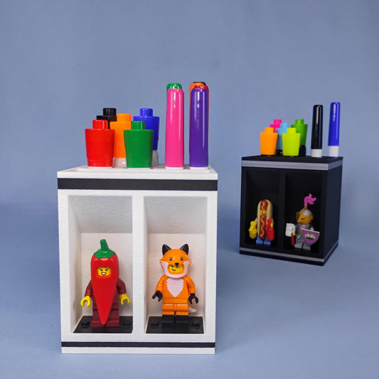 Black and white dry erase marker holders shown with colorful Expo-style markers and LEGO® minifigures. Each desktop organizer includes tiered marker storage and two front minifigure display bays.