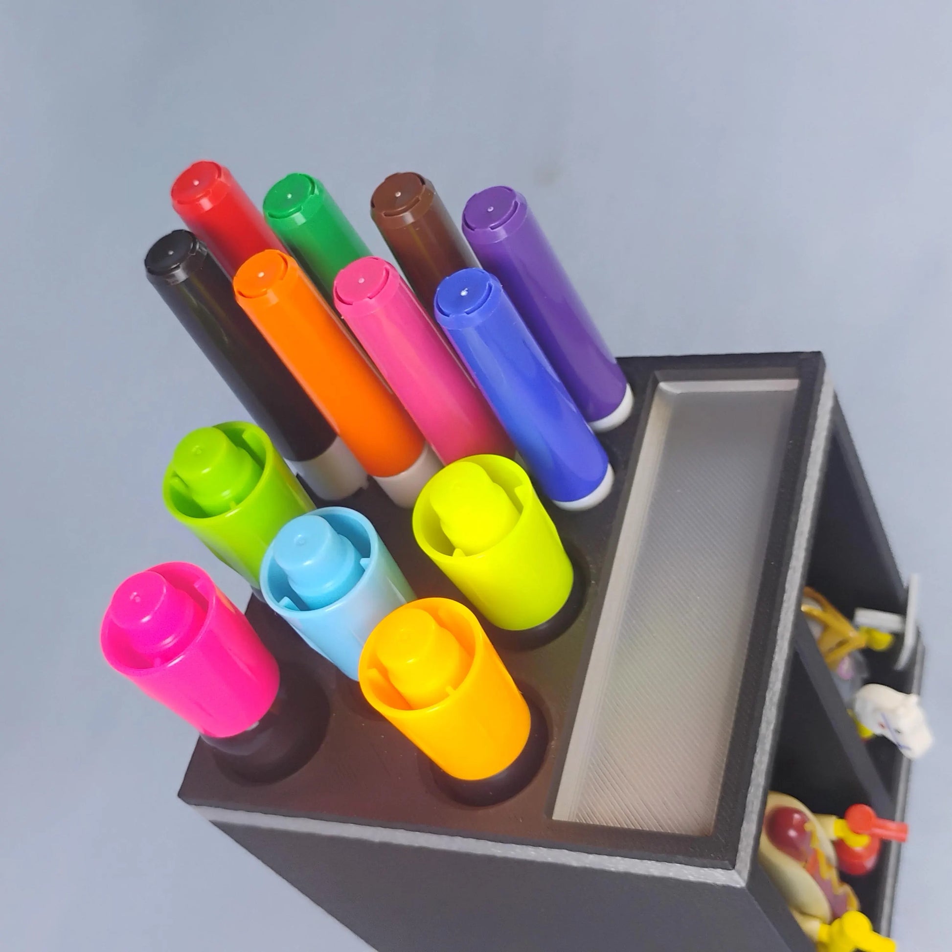 Top view of a black dry erase marker organizer holding large and fine-tip Expo-style markers, with an open top tray and front minifigure display bays.