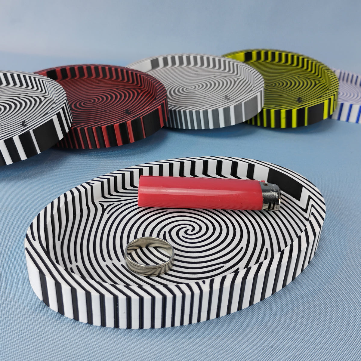 Fingerprint catchall trays in several color combinations, with a black and white tray holding a ring and red lighter.