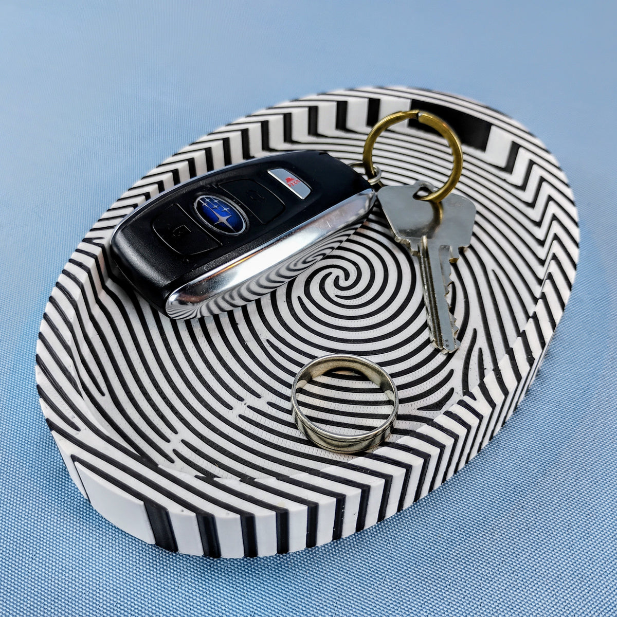 Black and white fingerprint catchall tray holding a car key fob, keys, and a ring on a blue background.