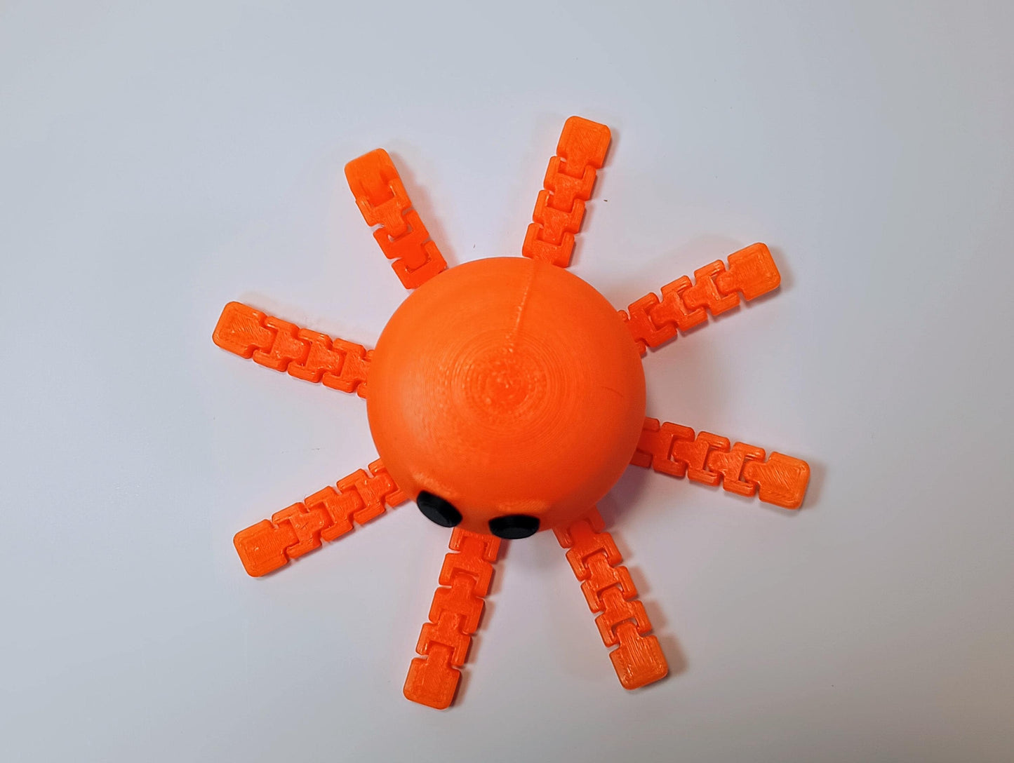 Top view of an orange flexi octopus figurine showing all eight articulated legs spread around the rounded body.