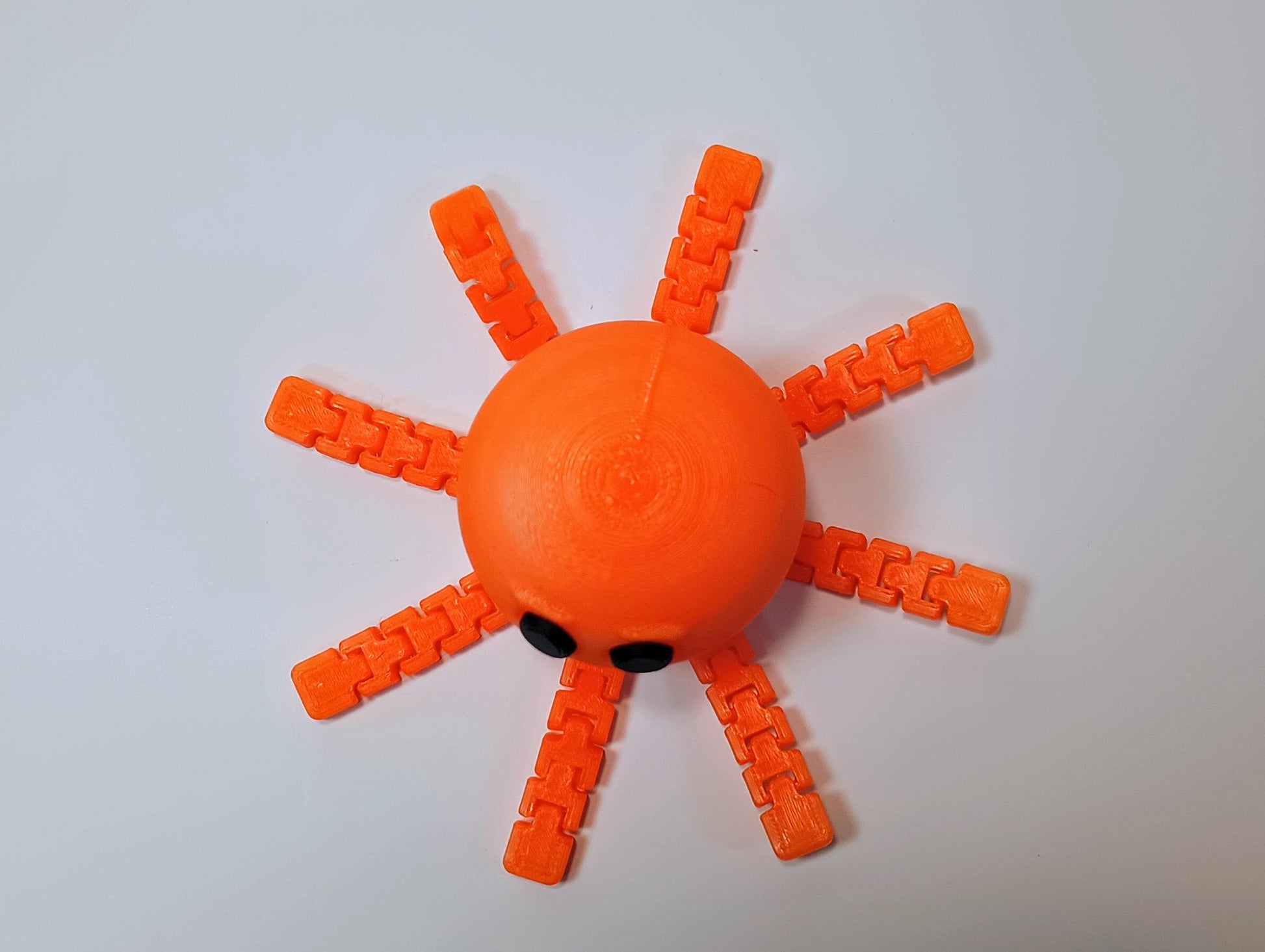 Top view of an orange flexi octopus figurine showing all eight articulated legs spread around the rounded body.