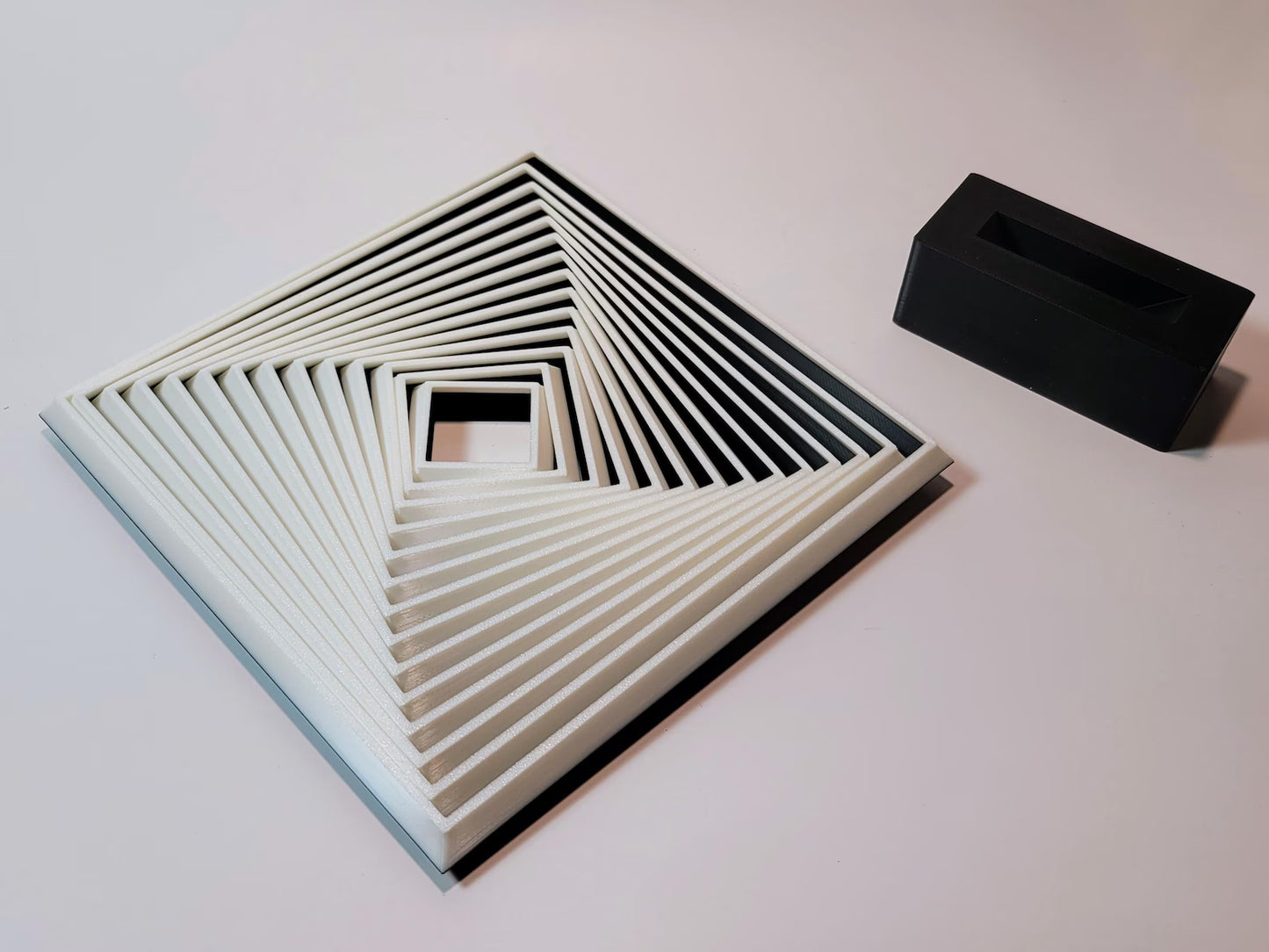 Large geometric fidget square shown flat beside its black display stand