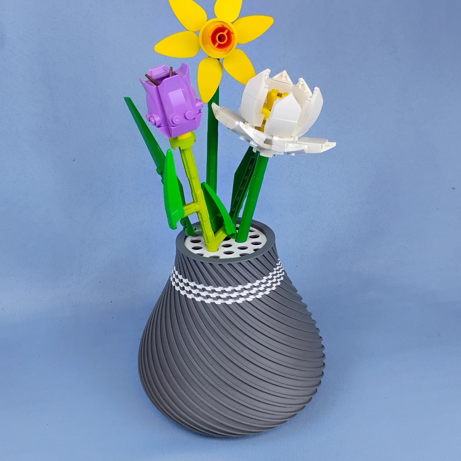 Gray swirly vase holding LEGO® botanical flowers on a blue background